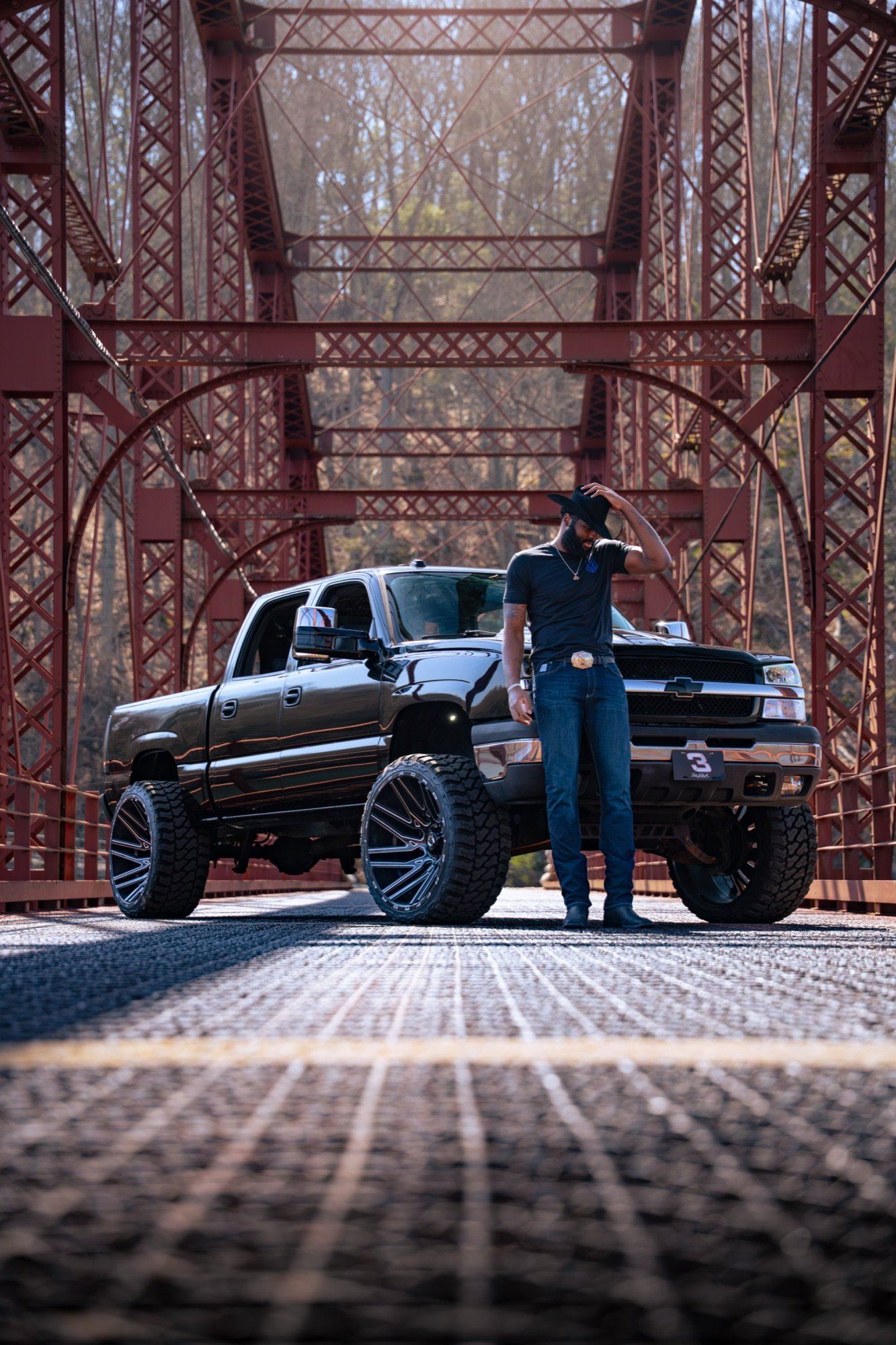 Cowboy hat on, leaning on the Cateye, red iron bridge behind